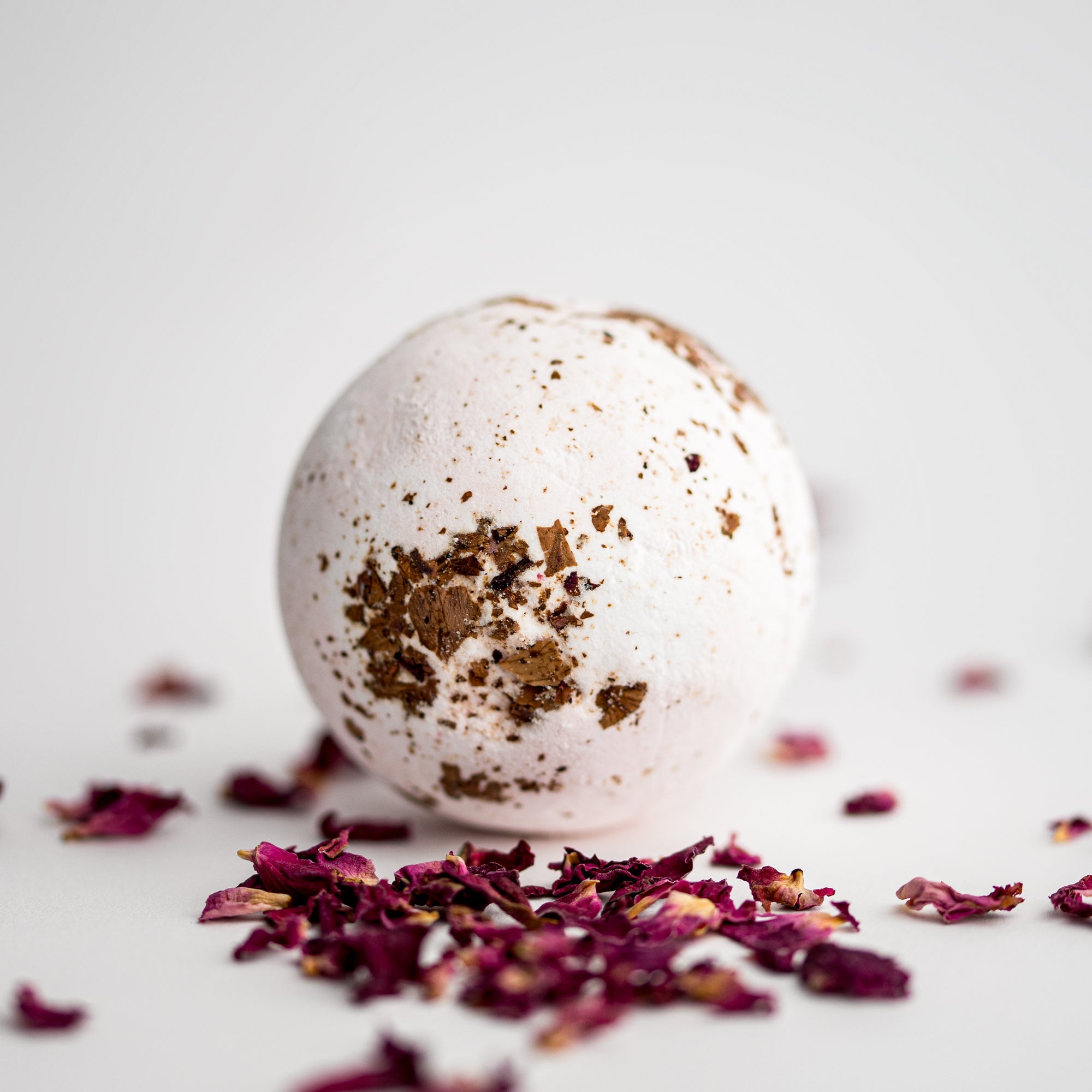 Rose Petal Bath Bomb, featured  surrounded by rose petals on a white background.