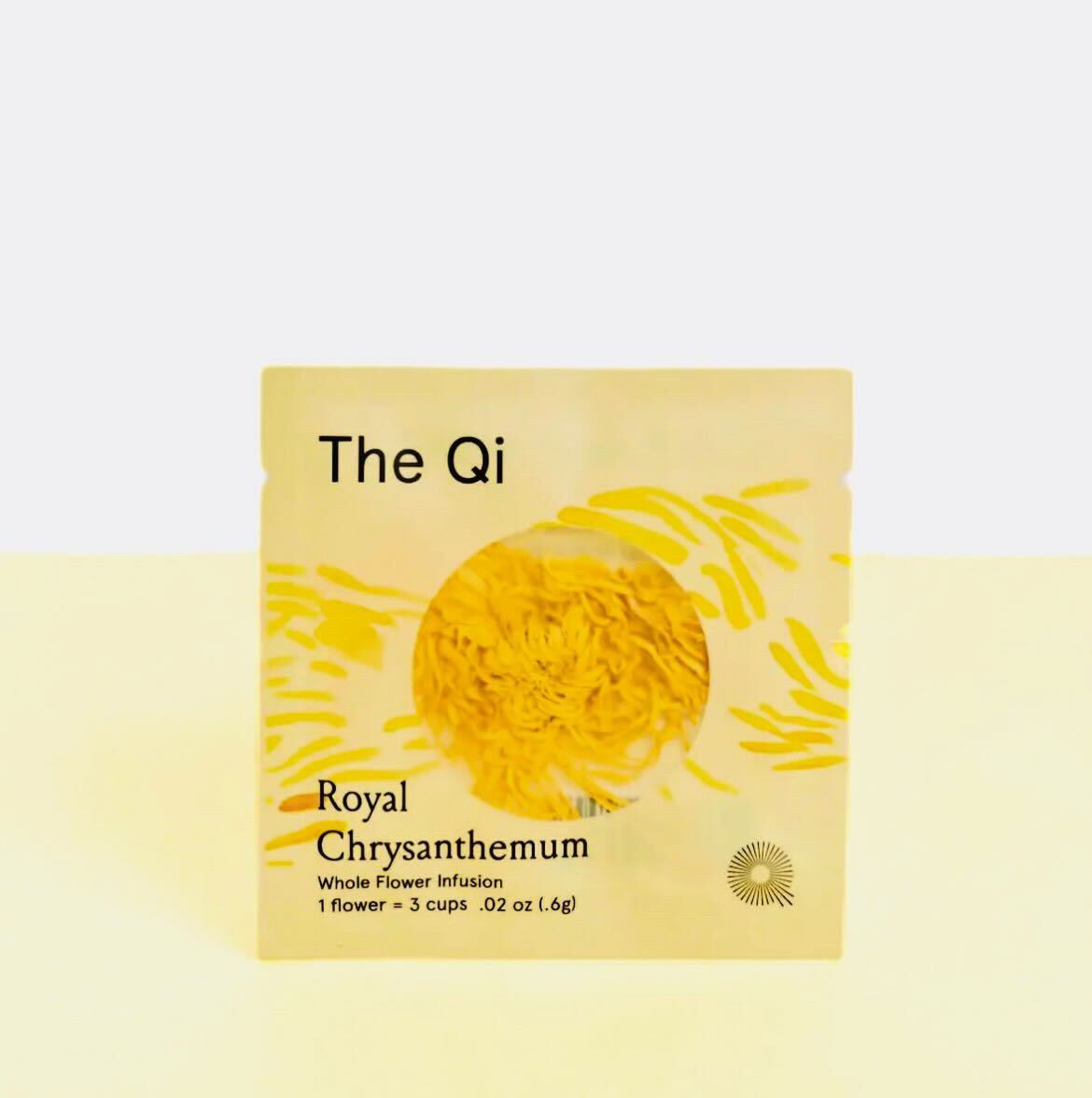 Royal Chrysanthemum whole flower infusion, image shows the package that the flower comes in, is a light yellow sachet with background image of pieces of the flower across it, revealing in a round transparent opening the sachet has the flower itself. 