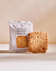 Rustic Bakery Salted Caramel Shortbread Cookie in its white packaging and outside of its packaging in a cream color background. 