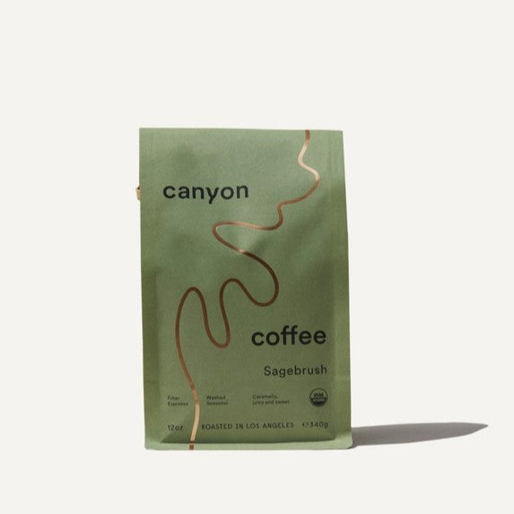 Sage brush canyon coffee is featured in its green package with a gold line detail and black lettering on a white background. 