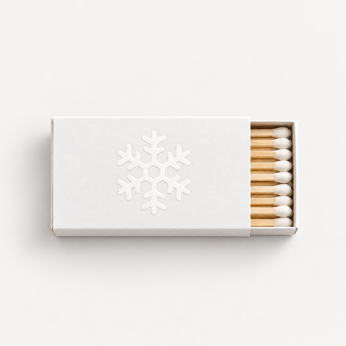 A minimalist white matchbox with a debossed snowflake design on the lid, shown partially open to reveal wooden matches with white tips, set against a clean white background.