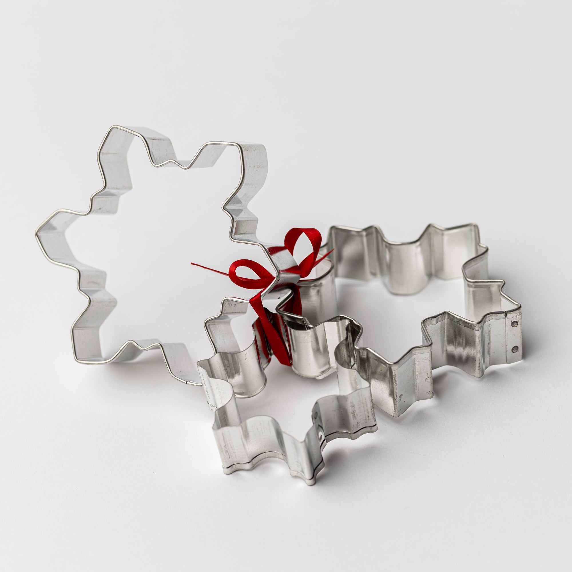 Two snowflake-shaped cookie cutters tied together with a red ribbon on a white background.
