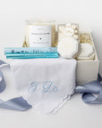 Front view of a “Something Blue” gift box displayed in a white box with a blue ribbon and ivory shred, containing an embroidered “I Do” handkerchief, a ring cleansing pen, a personalized velvet ring box, an 8oz “Bride’s Bouquet” personalized candle, and Mrs. Champagne Bubbles gummies.