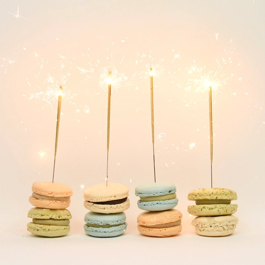 Photografic image featuring 4 of the sparklers on top of colorful macaroons on a pinkish background. 