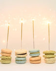 Photografic image featuring 4 of the sparklers on top of colorful macaroons on a pinkish background. 