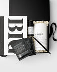 A curated gift set in a black box featuring a white and black Idea Book, a white CAMPO diffuser, two black COOFIE medium roasted coffee sachets, and a black pen, arranged on a light gray background.