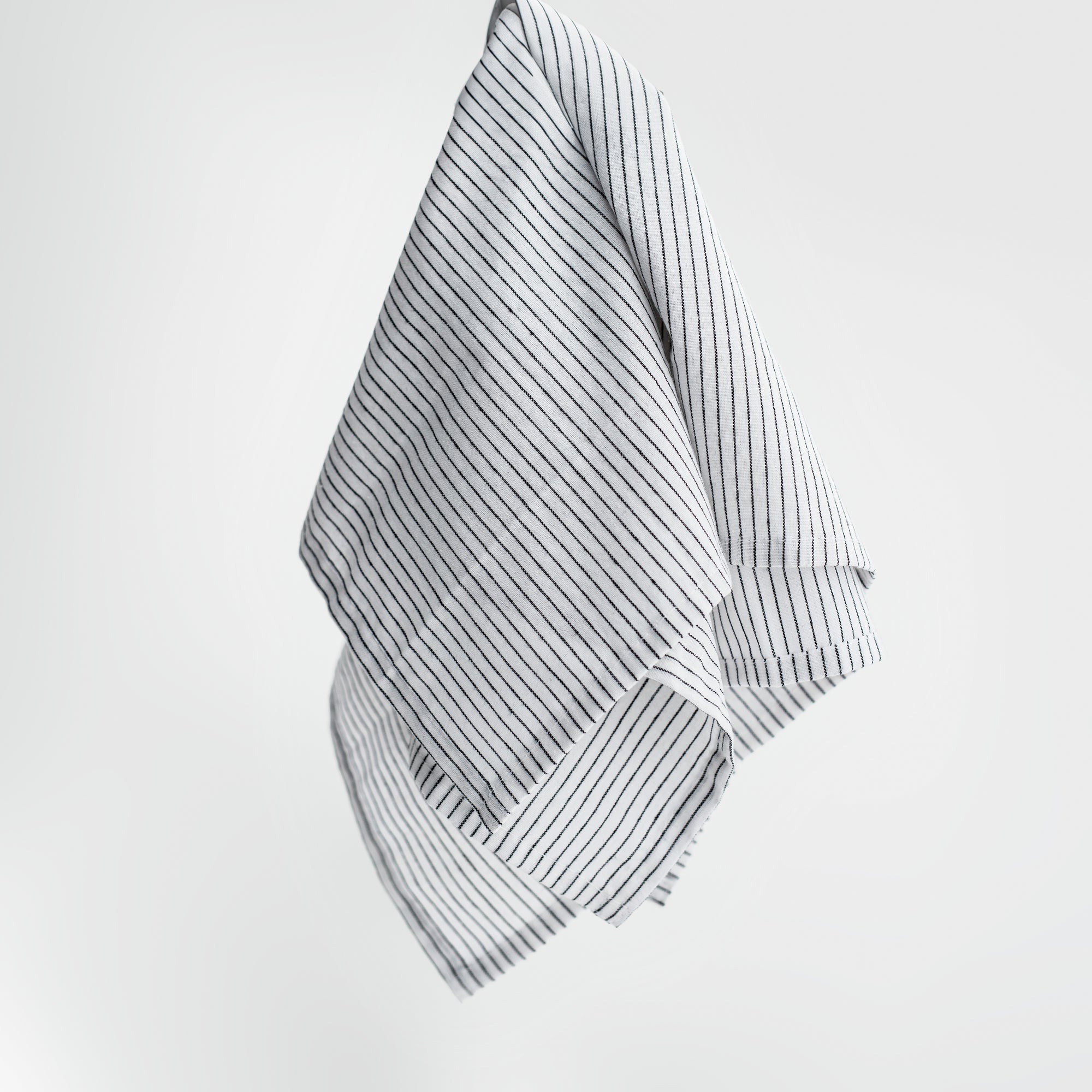 Stripped linen kitchen towel featured in its white and black lines design on a white background. 