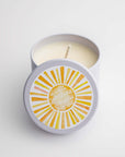 Sunshine natural soy candle in its white ceramic jar and white round label on top of the lid with a sun and in white lettering in the middle of it a little sunshine to brighten your day on a white background. 