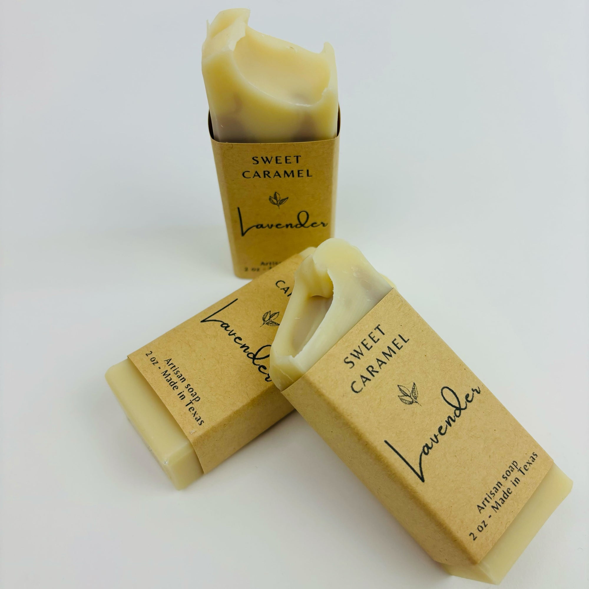 Three bars of light beige/cream-colored soap, lavender, wrapped in kraft paper, are displayed against a plain white background.