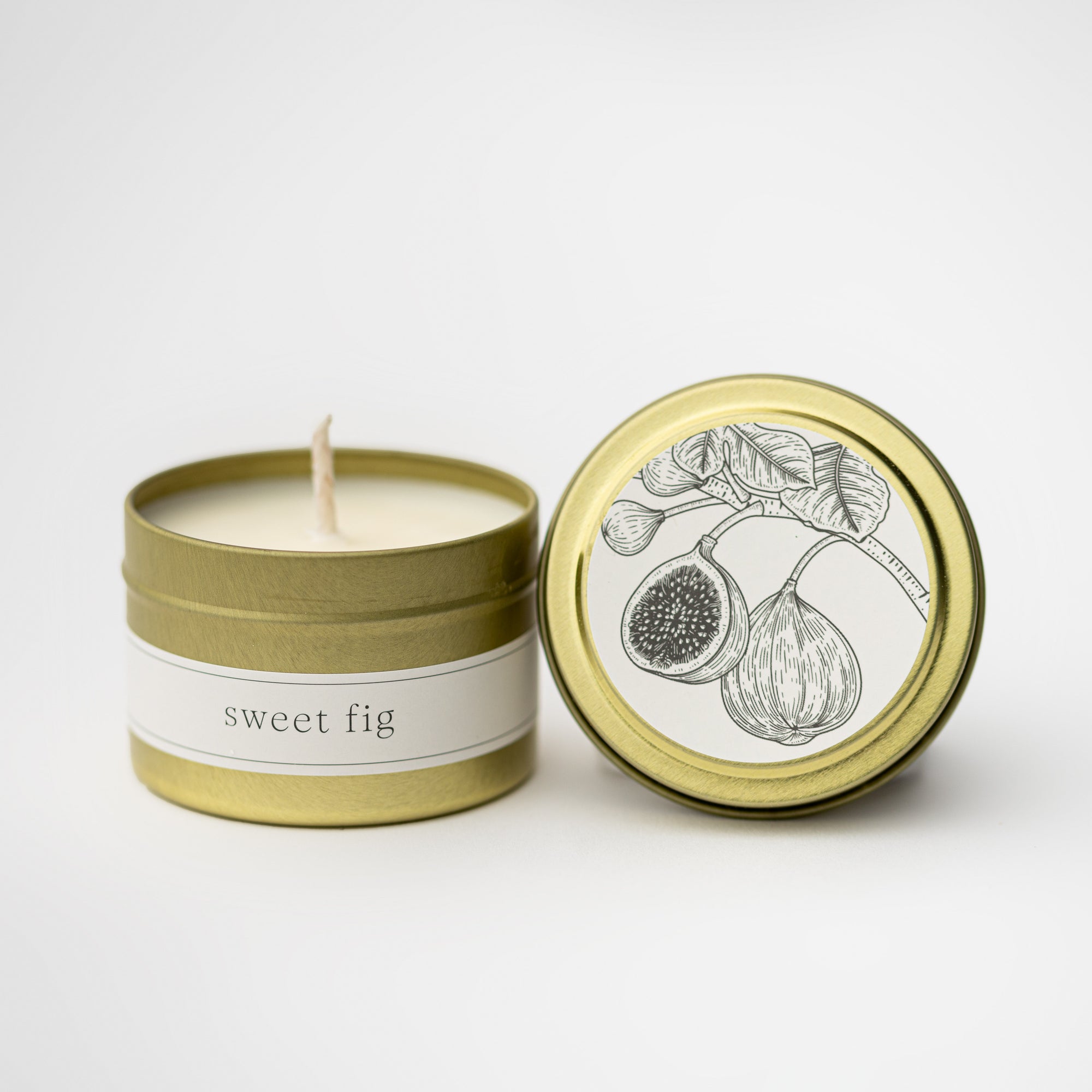Sweet fig travel size candle in our signature gold tin with white label on top round and fig illustration and in the tin in black lettering sweet fig on a white background.  