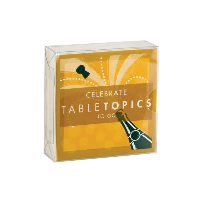 A box of cards, featuring a champagne bottle design, is presented against a plain white background. The box is a clear plastic covering a card with a design featuring a champagne bottle with a cork popping out, surrounded by celebratory dots and lines.  The words "CELEBRATE", "TABLETOPICS", and "TO GO" are printed on the card, in a bold and stylized font
