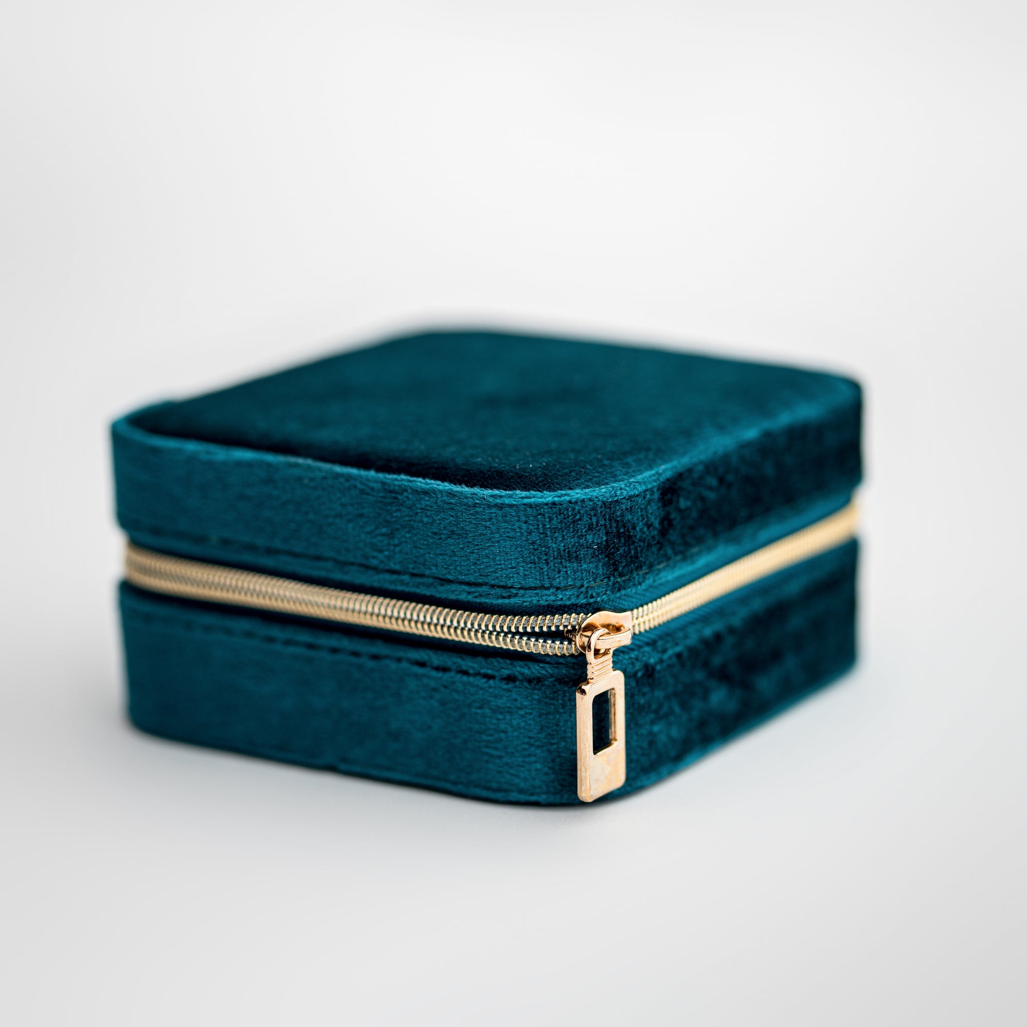 Teal velvet jewelry box, image presents a close-up shot of a rectangular, teal velvet jewelry box with a gold-toned zipper.