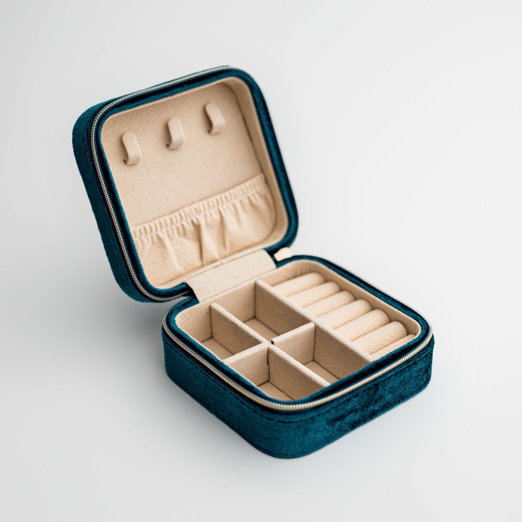 Teal velvet jewelry box, close-up photograph showcases an teal velvet jewelry box, opened to display its beige interior compartments and organizers, set against a clean white backdrop.