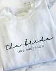 The bride custom name sweatshirt in white personalized in black lettering the bride Mrs. Anderson in a marble-liked background.
