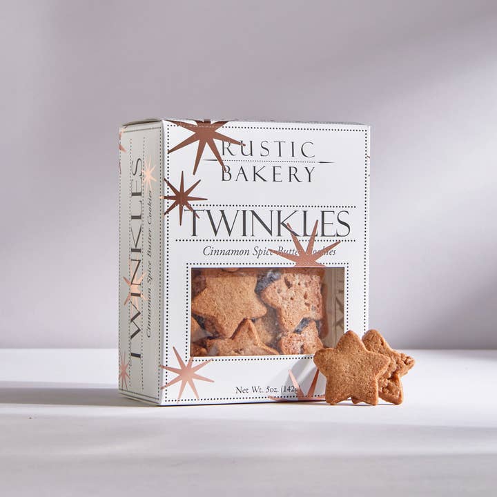 Twinkles cinnamon spice butter cookies is featured in its square-shaped package white with brown stars and black lettering. Wit two of the star shaped cookies outside of the box on a white background. 