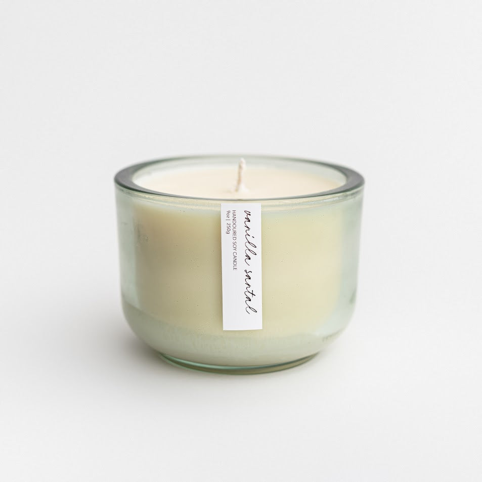 Vanilla Santal luxury candle in its green jar container on a white background. 