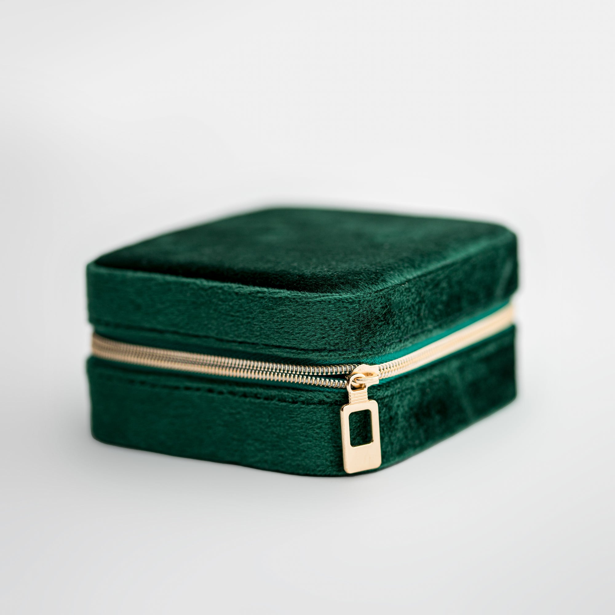 Emerald velvet jewelry box, image presents a close-up shot of a rectangular, emerald-green velvet jewelry box with a gold-toned zipper.