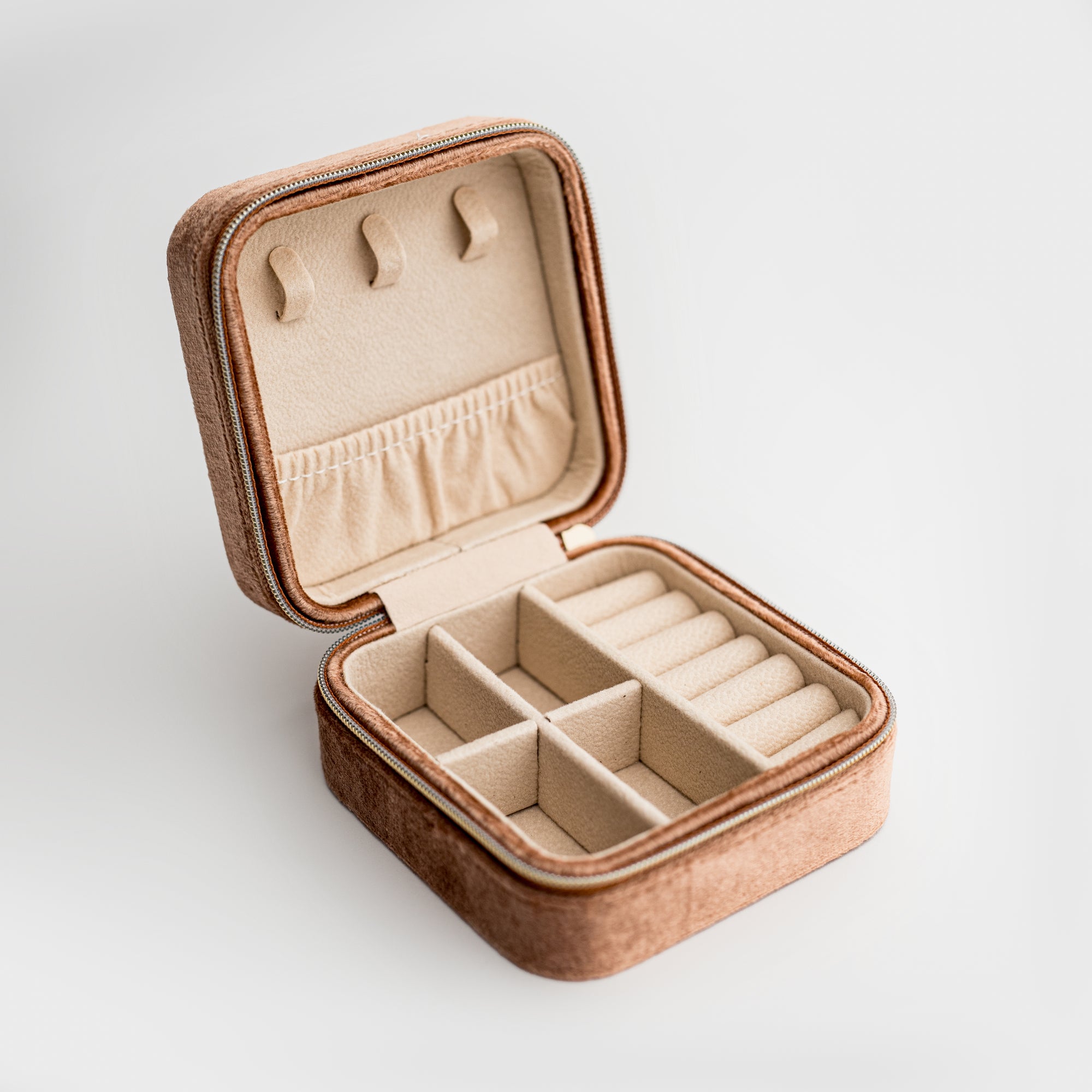 Showcased velvet jewelry box in taupe color open showing its division and light brown color in the inside on a white background. 