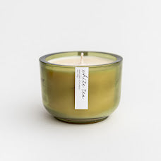 White tea luxury candle featured in its green glass container on a white background. 