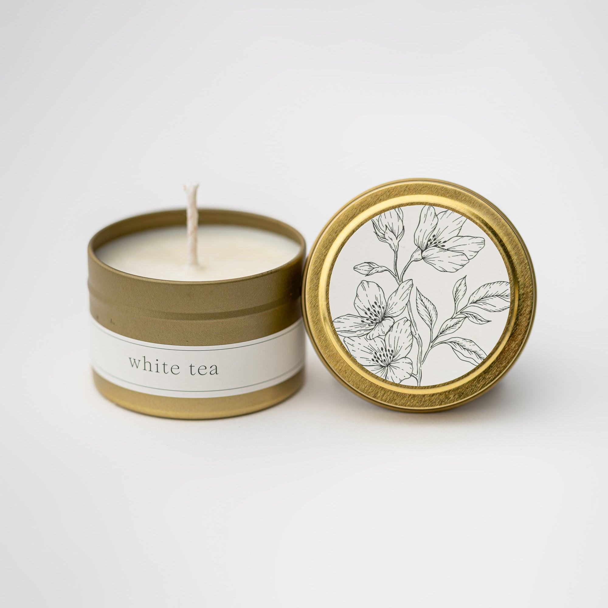 White tea travel size candle in our signature gold tin with white label on lid and tin with a floral design and black lettering.   