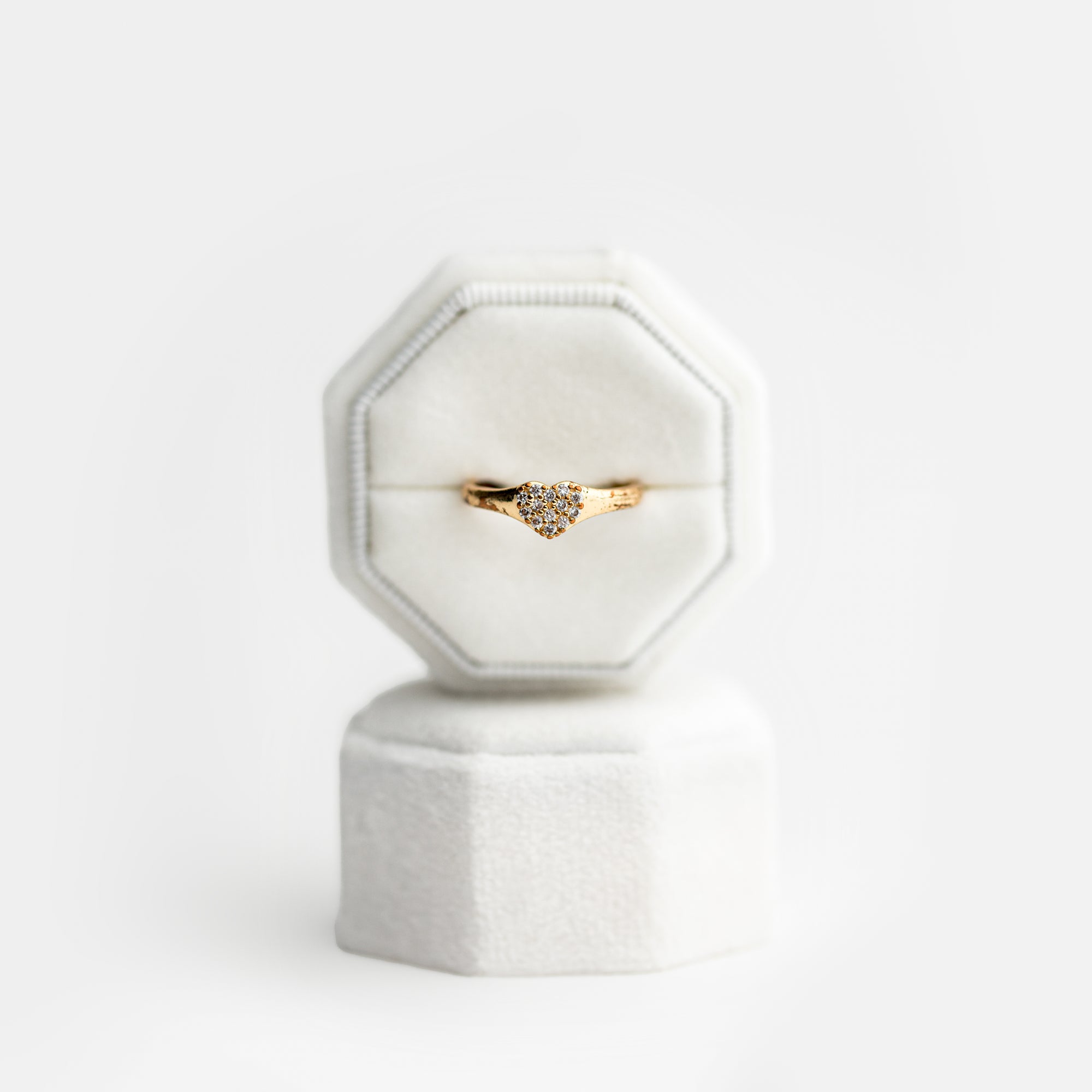 White velvet ring box with a gold heart-shaped ring with diamonds and brown gemstones on a white background. 