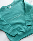 Youth custom embroidered teal with white “custom” text ona marble background. 