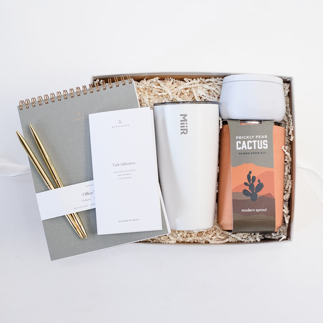 8" spiral top bound grey Appointed Notebook, teakwood & cardamom 8 oz white candle, appointed task adhesives, Modern Sprout Prickly Pear Cactus grow kit in terracotta pot, 16 oz white Miir Tumbler, and set of two gold pens in a light grey gift box.