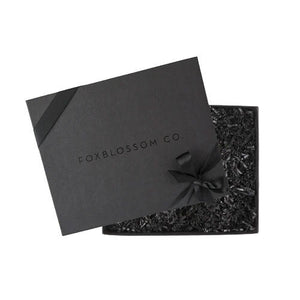 Black box embossed with foxblossom co. filled with black paper shred and tied with black ribbon.