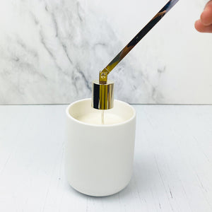 Gold plated candle snuffer being used to put out wick in a white ceramic jar