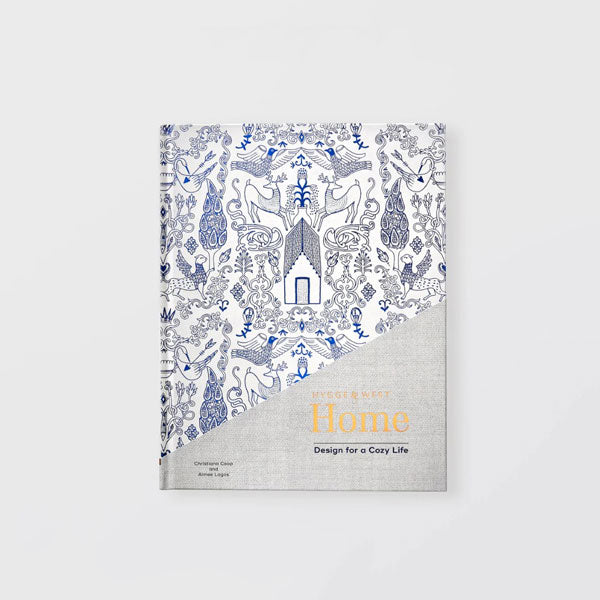 Hygge &West Home, Design for a cozy life book featured on a white background. The books hard cover is images in blue and silver lines. 