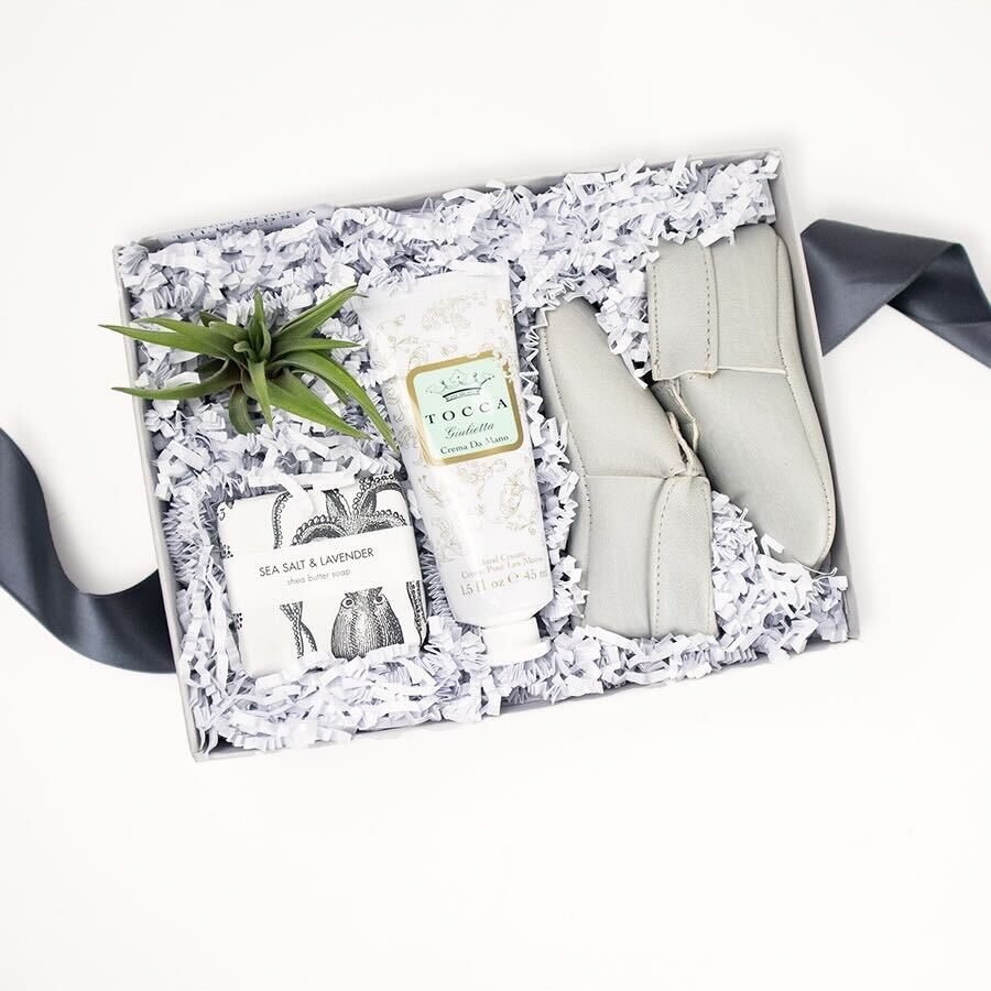 Light grey gift box with Sweet n' Swag modern mox baby shoes, Tocca Giulietta hand cream, a small air plant, and Formulary 55 Sea Salt & Lavender shea butter soap.