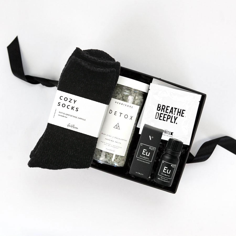 Black chenille socks, Herbivore detox bath salts, vitruvi eucalyptus essential oil, Spritz breathe deeply set of three wipes in a black box.