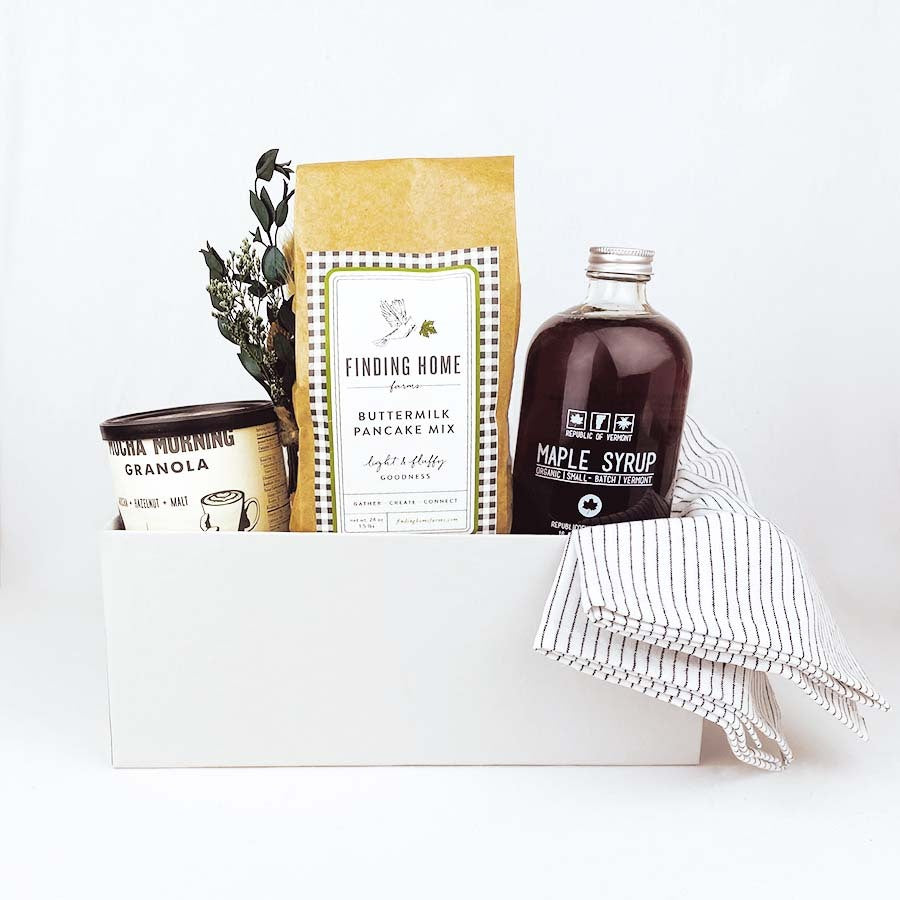 Light grey box containing white linen tea towel with black stripes, glass bottle of vermont maple syrup, can of mocha morning granola, bag of buttermilk pancake mix and dried floral bundle.