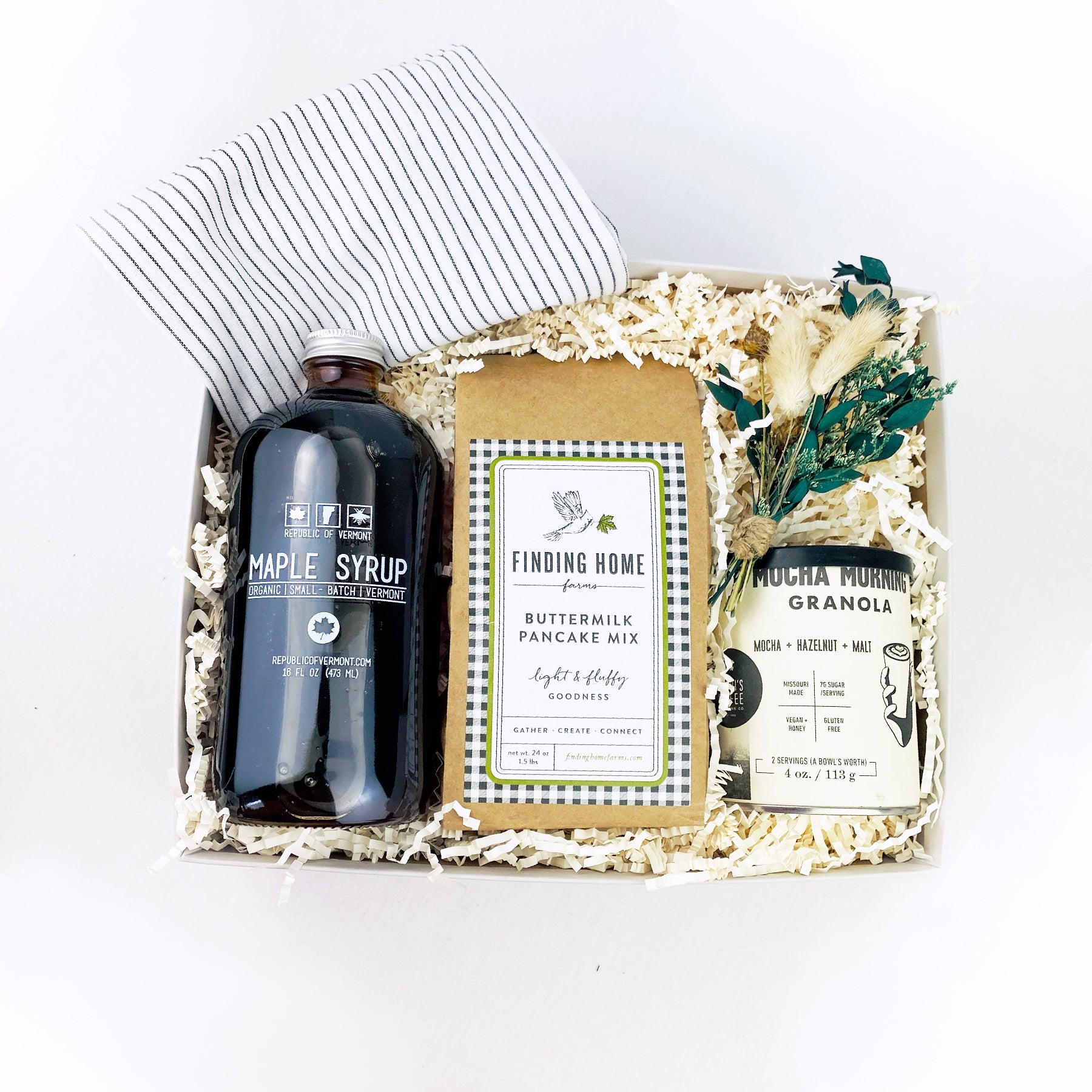 Light grey box containing white linen tea towel with black stripes, glass bottle of vermont maple syrup, can of mocha morning granola, bag of buttermilk pancake mix and dried floral bundle.