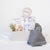A light gray gifting box with a dried floral bundle, Slumberkins Slumber Sloth and hardback book, Chelsey Wang night night baby wash, a charcoal muslin swaddle and silicone and wooden teether.