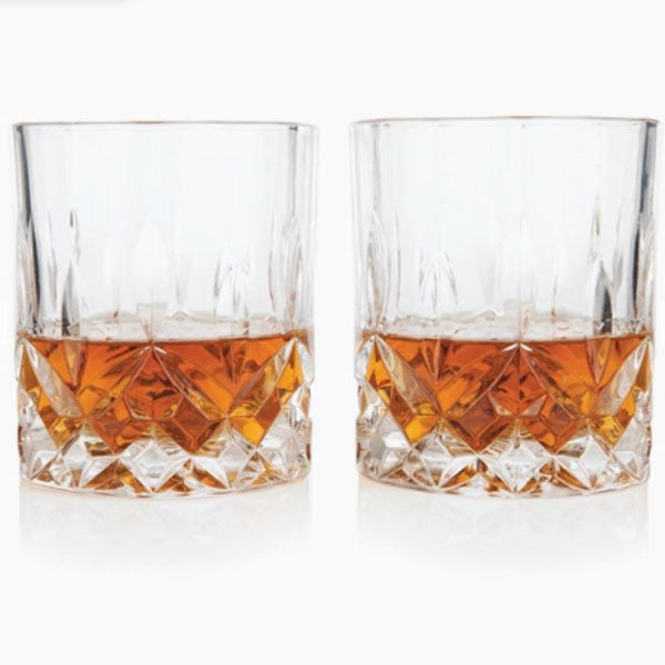 Two crystal glasses with faceted detail containing whiskey placed next to each other.