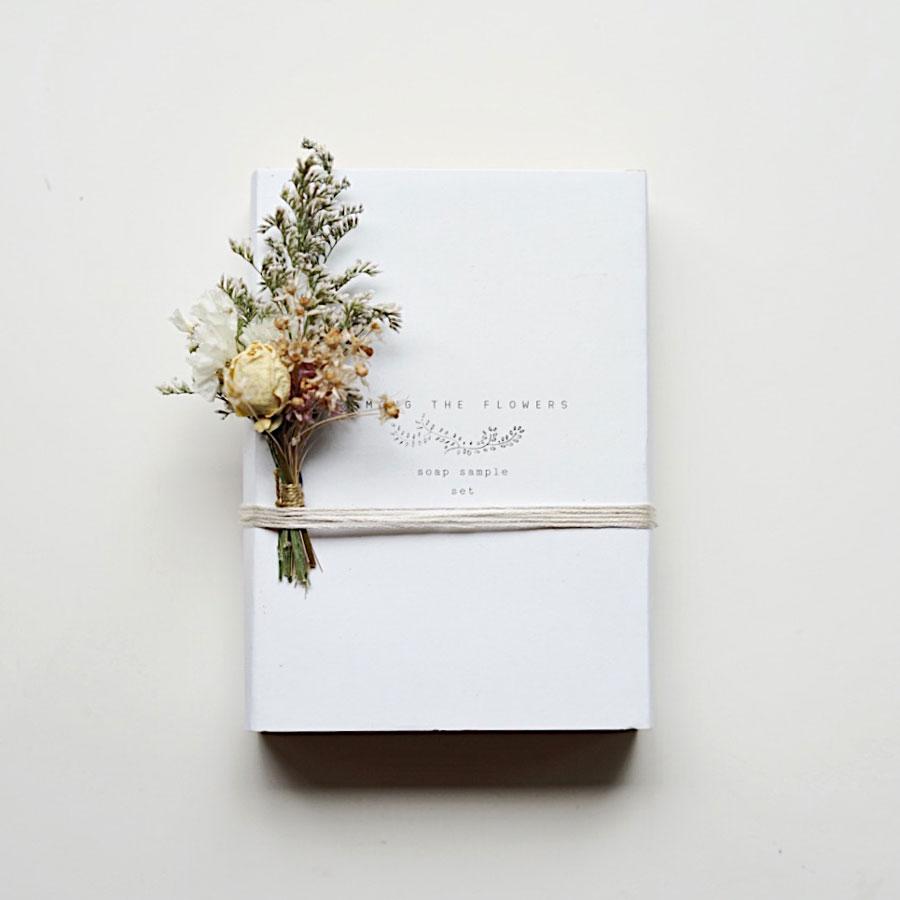 White rectangular box with black text centered, string wrapped around lower part of box (color of string varies), floral stem tucked into the string on one side. 