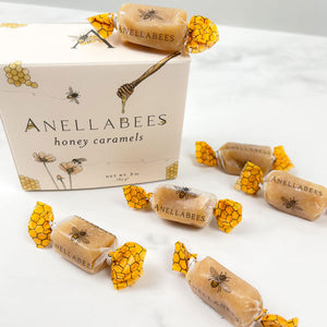 Cream/yellowish toned box. drawings of honey combs, bees, flowers, and honey stir on front. "Annellabees, honey caramels" (brand/product) and serving amount on front. Caramel candy pieces, twisted with yellow honey comb end twisted wrapping.