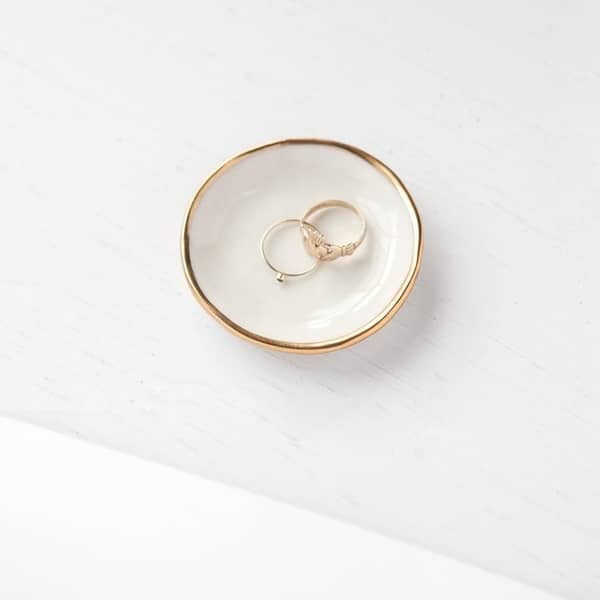White ceramic ring dish, gold trimming. Holding two gold rings. 