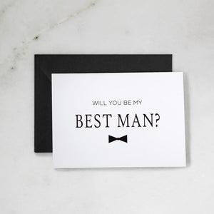White envelope size card (approx. 3.5" x 5"), reads, "Will you be my best man?" in black text with a black bowtie graphic. Black envelope behind. 