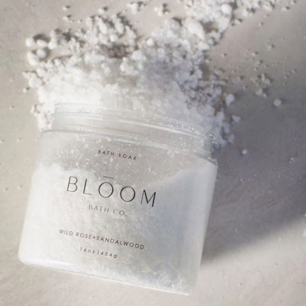 Image of the bloom wild rose and sandalwood bath soak opened showing it's transparent jar and white salts. 