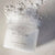 White, textured grapefruit scrub in a clear glass jar, black twist off top, black text. Comes in a light pink box, black text. 