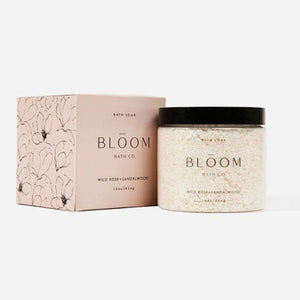 White, textured grapefruit scrub in a clear glass jar, black twist off top, black text. Comes in a light pink box, black text. 
