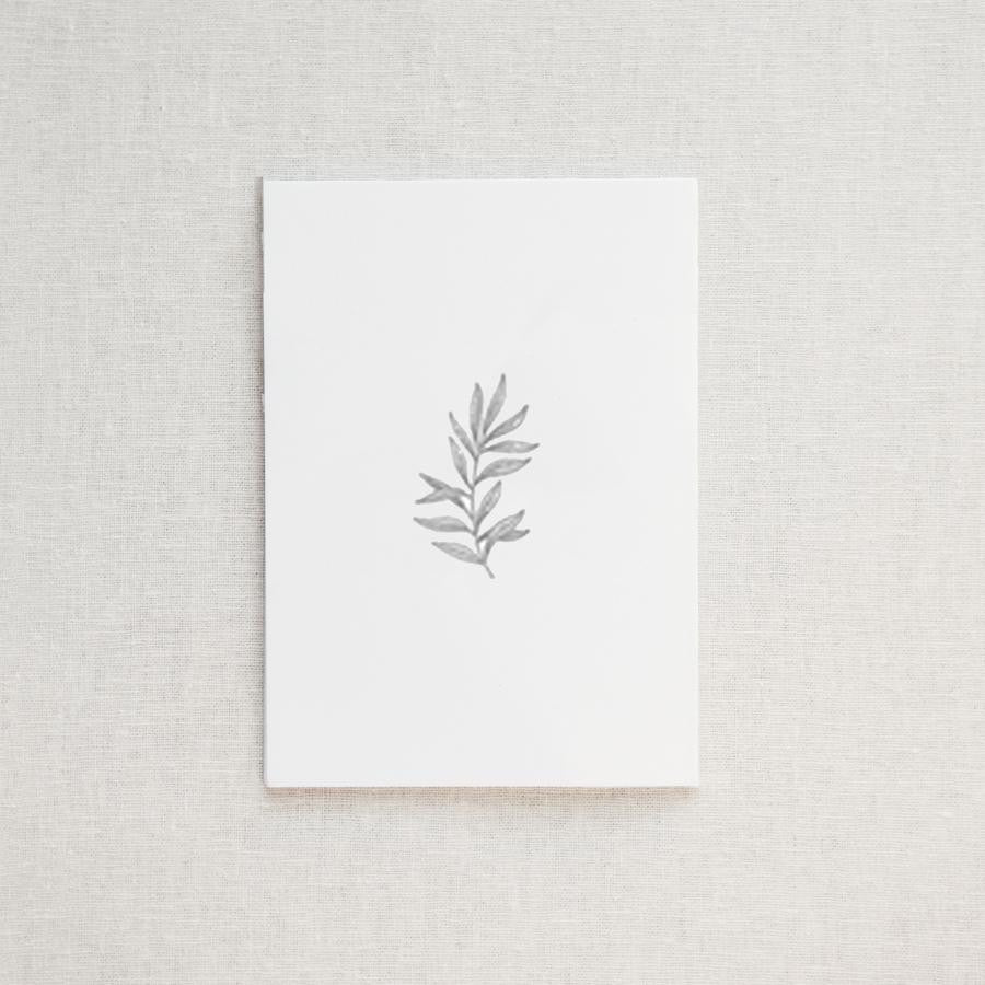 Our botanical card is featured. A minimalist, monochromatic sketch presents a sprig of delicate leaves centered on a stark white rectangular card, set against a neutral, textured backdrop.