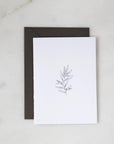 Our botanical card is featured. A minimalist, monochromatic sketch presents a sprig of delicate leaves centered on a stark white rectangular card, set against a marble-like backdrop.