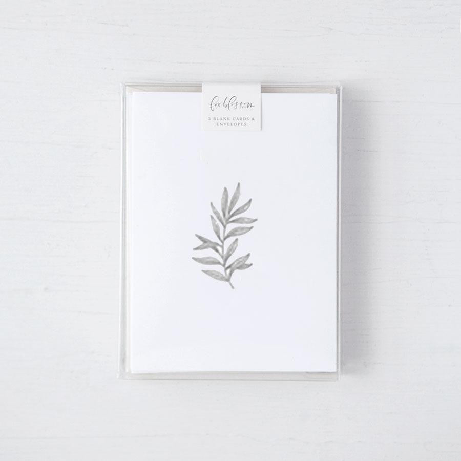 Our botanical card box set is featured. A minimalist, monochromatic sketch presents a sprig of delicate leaves centered on a stark white rectangular card, set against a neutral, textured backdrop.