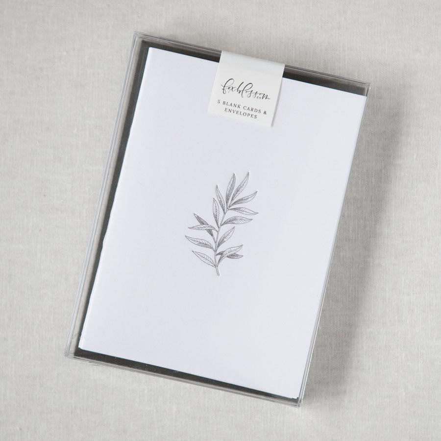 Our botanical card box set is featured. A minimalist, monochromatic sketch presents a sprig of delicate leaves centered on a stark white rectangular card, set against a neutral, textured backdrop.