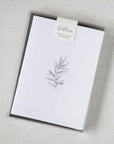 Our botanical card box set is featured. A minimalist, monochromatic sketch presents a sprig of delicate leaves centered on a stark white rectangular card, set against a neutral, textured backdrop.