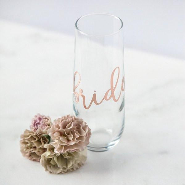 Personalized stemless glass flute with "bride" in rose gold script with roses next to it in a marble-like background. 