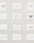  Display of twelve white cards. Gold floral heart, pink xoxo, gray branch, white congrats embossed, happy birthday under five candles, thank you in gray script, thinking of you, I couldn't tie the knot without you in gold, Yay! in gold script, will you be my bridesmaid rose gold, will you be my maid of honor rose gold, will you be my matron of honor rose gold